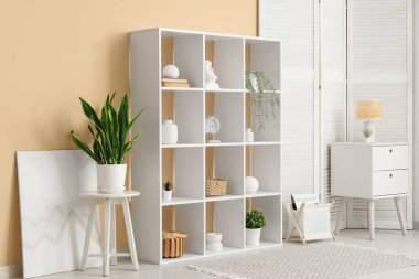 Oturma odasının içinde beyaz raf ünitesi, katlanır ekran ve masa