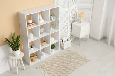 Oturma odasının içinde beyaz raf ünitesi, katlanır ekran ve masa