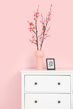 Çiçek açan dalları ve pembe duvarın yanındaki tuvalette çerçevesi olan vazo.