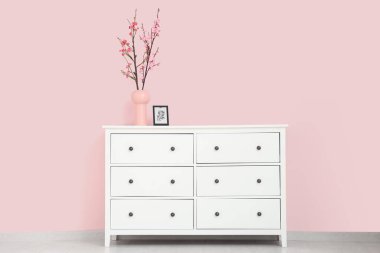 Çiçek açan dalları olan bir vazo ve odada pembe duvarın yanındaki klozetin üzerindeki çerçeve.