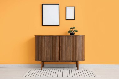 Bonsai ağacıyla klozet ve odanın sarı duvarında boş çerçeveler