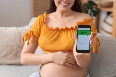 Glikoz sensörü ve cep telefonu olan genç hamile bir kadın kan şekerini ölçüyor, yakın plan. Gebelik Diyabet Konsepti