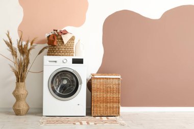 Çamaşır sepetli modern çamaşır makinesi ve vazoda renkli duvarın yanındaki vazoda otlar.