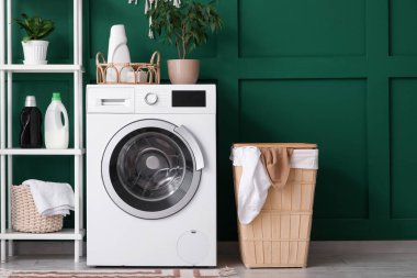 Modern çamaşır makinesi, raf ünitesi ve yeşil duvarın yanındaki çamaşır sepeti.