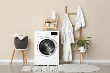 Çamaşır makinesi, kirli elbiseli sepet ve çamaşır odasında bornozlu merdiven.