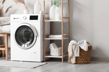 Modern çamaşır makinesi, raf ünitesi ve çamaşır sepeti banyoda beyaz duvarın yanında.