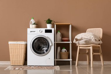 Modern çamaşır makinesi, banyoda deterjan ve çamaşır sepeti olan raf ünitesi.