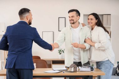 Erkek emlakçı ve ofiste el sıkışan evden anahtarı olan hamile bir çift.