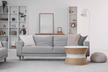 Gri kanepe, rattan masa ve raf üniteleriyle aydınlık oturma odasının içinde.