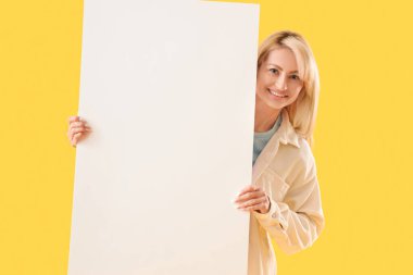 Sarı arka planda boş posteri olan güzel bir kadın.