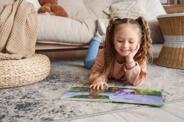 Evdeki halıda kitap okuyan tatlı küçük bir kız.