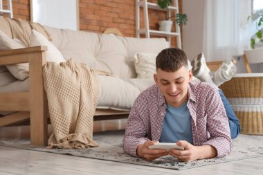 Evdeki halıda cep telefonu kullanan genç adam.