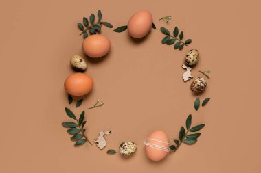 Paskalya yumurtalarından yapılmış bir çerçeve ve kahverengi arka planda ahşap tavşanlar.