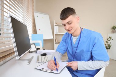 Klinikteki masada panoya yazan erkek stajyer doktor.