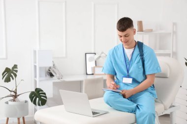 Klinikte dizüstü bilgisayarla çalışan bir erkek stajyer.