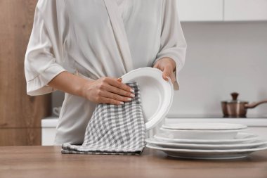 Genç bir kadın, mutfakta peçeteyle tabağı siliyor.