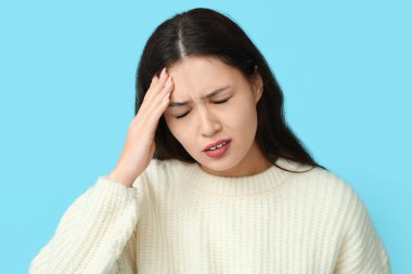 Mavi arka planda baş ağrısı çeken genç bir Asyalı kadın. Beyin Sakatlığı Bilinci Ayı