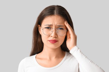 Genç Asyalı kadın gri arka planda baş ağrısı çekiyor. Beyin Sakatlığı Bilinci Ayı