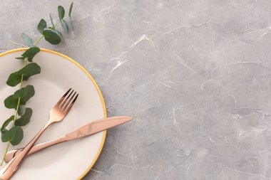 Gri grunge arka planda tabak, çatal bıçak ve okaliptüs dallarıyla şık masa ayarları