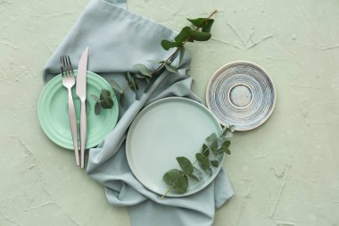 Yeşil grunge arka planında tabak, çatal bıçak ve okaliptüs dallarıyla şık masa ayarları