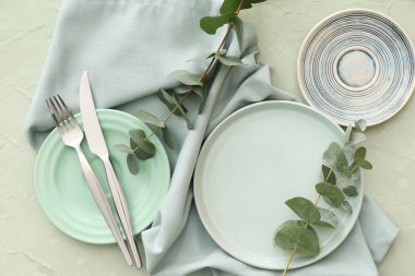 Yeşil grunge arka planında tabak, çatal bıçak ve okaliptüs dallarıyla şık masa ayarları