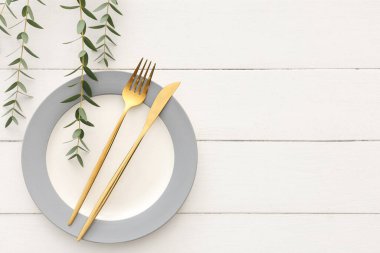 Beyaz ahşap arka planda tabak, çatal bıçak ve bitki dallarıyla şık bir masa.