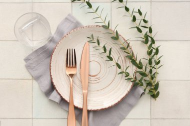 Tabak, çatal bıçak, peçete, cam ve bitki dallarıyla süslü şık masa seti.