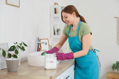 Sünger ve kabartma tozu temizleme lavabosu olan genç bir kadın.