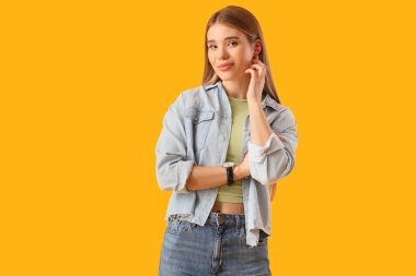 Sarı arka planda kulak tıkacı olan genç bir kadın.