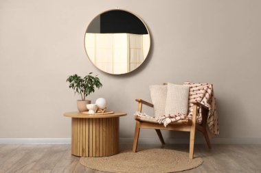 Gri duvardaki ayna, odanın içindeki masa ve koltuk.