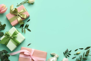 Dekoratif tavşancıktan yapılmış çerçeve, hediye kutuları, çiçekler ve turkuaz arka planda yeşil yapraklar. Paskalya kutlaması