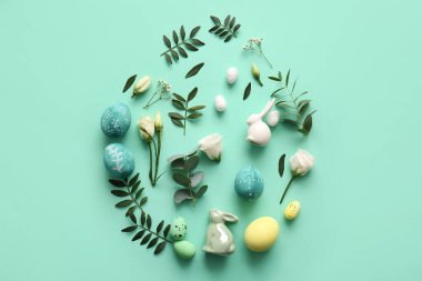 Paskalya yumurtaları, dekoratif tavşanlar, çiçekler ve turkuaz arka planda yeşil yapraklarla kompozisyon