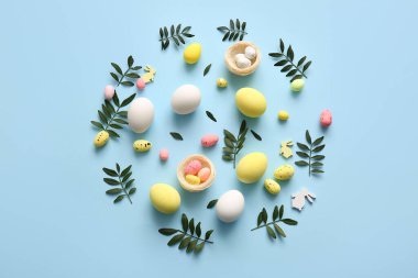 Paskalya yumurtaları, dekoratif yuvaları ve mavi arka planda yeşil yapraklarla kompozisyon