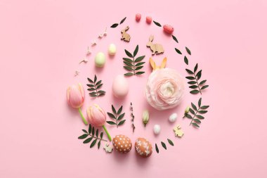Paskalya yumurtaları, dekoratif tavşanlar, çiçekler ve pembe arka planda yumurta şeklinde yeşil yapraklar.