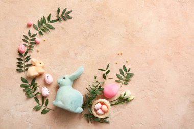 Paskalya yumurtaları, dekoratif yuva, tavşanlar ve bej rengi grunge arka planda yeşil yapraklardan yapılmış çerçeve.