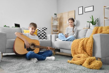 Gitar çalan genç bir çocuk ve evde cep telefonu kullanan kulaklıklı bir kız kardeşi var.