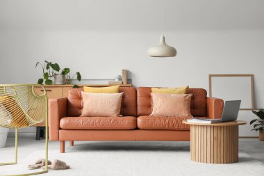 Kahve masasında kahverengi deri kanepe, koltuk ve dizüstü bilgisayar olan oturma odası.