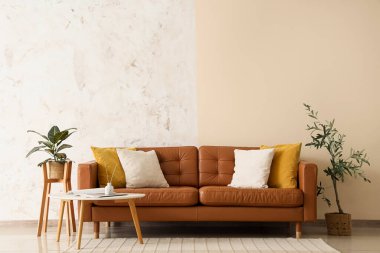 Oturma odasının içinde kahverengi deri kanepe, ev bitkileri ve grunge duvarının yanında kahve masası.