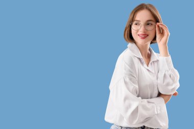 Mavi arka planda yeni gözlüklü güzel, genç ve mutlu bir kadın.