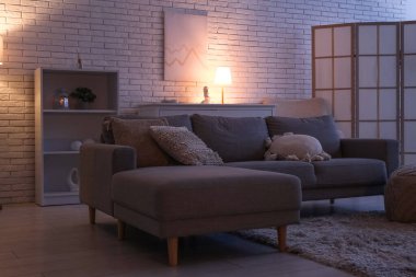 Beyaz tuğla duvarın yanında, kanepesi ve parlak lambaları olan karanlık oturma odasının içinde.