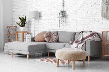 Beyaz tuğla duvarın yanında puf ve kanepe olan aydınlık oturma odasının içinde.