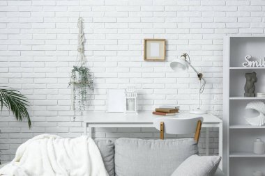 Açık oturma odasındaki beyaz tuğla duvarın yanında kitap ve lambalar olan masa.