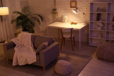 Beyaz tuğla duvarın yanında kanepe, masa, sandalye ve parlayan lambalar olan karanlık oturma odasının içinde.