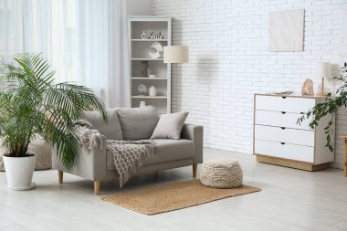 Beyaz tuğla duvarın yanında kanepe, puf ve sandıklı aydınlık oturma odasının içinde.