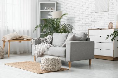 Beyaz tuğla duvarın yanında kanepe, puf ve sandıklı aydınlık oturma odasının içinde.