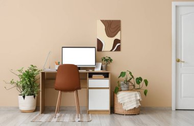 Modern bilgisayar ve bej duvarın yanındaki ev bitkileriyle lüks çalışma alanı