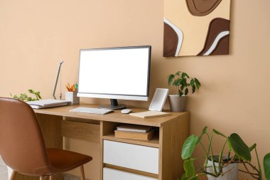 Modern bilgisayar ve bej duvarın yanındaki ev bitkileriyle lüks çalışma alanı