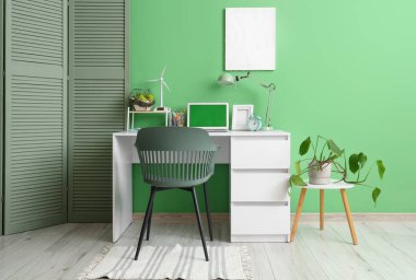 Modern dizüstü bilgisayarı ve yeşil duvarın yanındaki masa lambası ile şık çalışma alanı