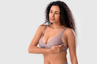 Genç Afro-Amerikalı kadın göğsünü beyaz arka planda kontrol ediyor. Kanser farkındalığı kavramı