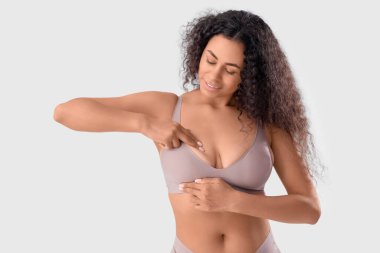 Genç Afro-Amerikalı kadın göğsünü beyaz arka planda kontrol ediyor. Kanser farkındalığı kavramı